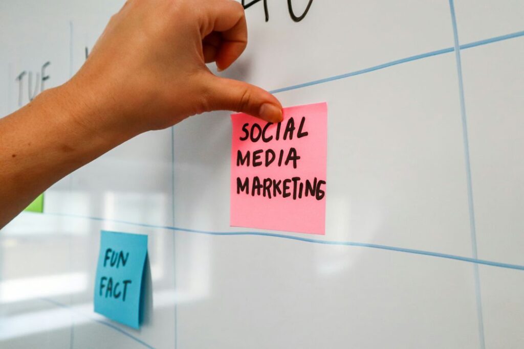 Close up of a hand sticking a pink sticky note reading social media marketing, onto a white board