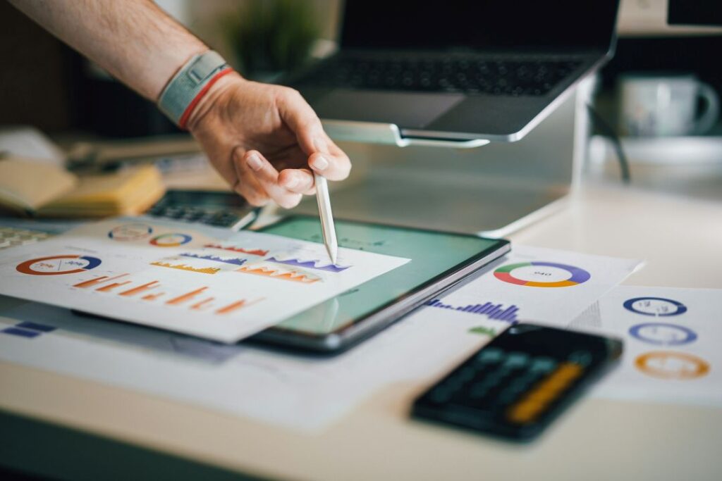 A hand holding a pencil is hovering above a printed sheet of marketing charts.