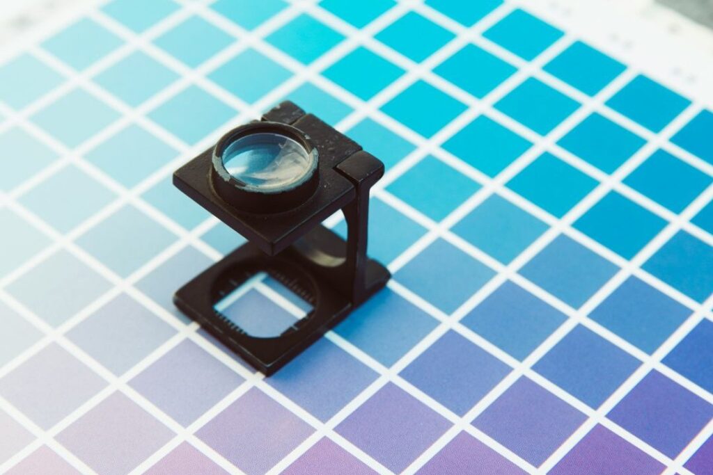 A magnifying viewer sits on top of a sheet of paper printed with small squares each similar in colour but slightly different gradients.