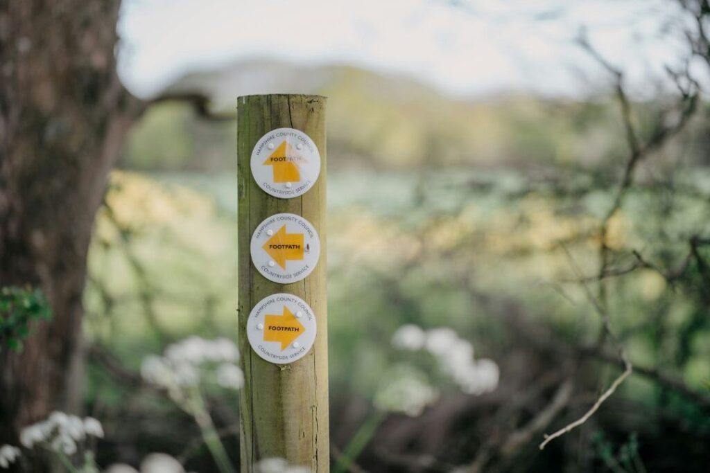 In focus is a waymarker post with three footpath arrows pointing in different directions
